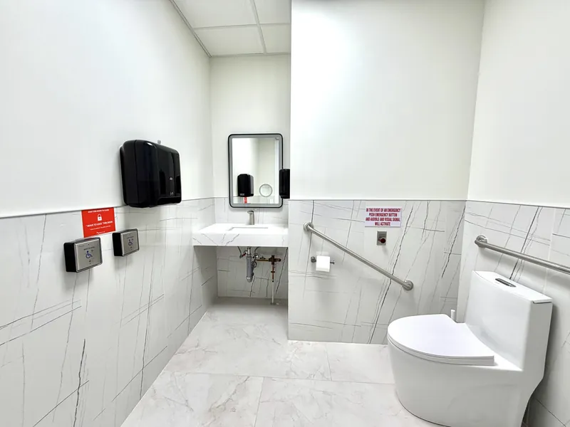 Accessible washroom with stainless grab bars, a floating quartz vanity, touchless door controls and porcelain wall tile
